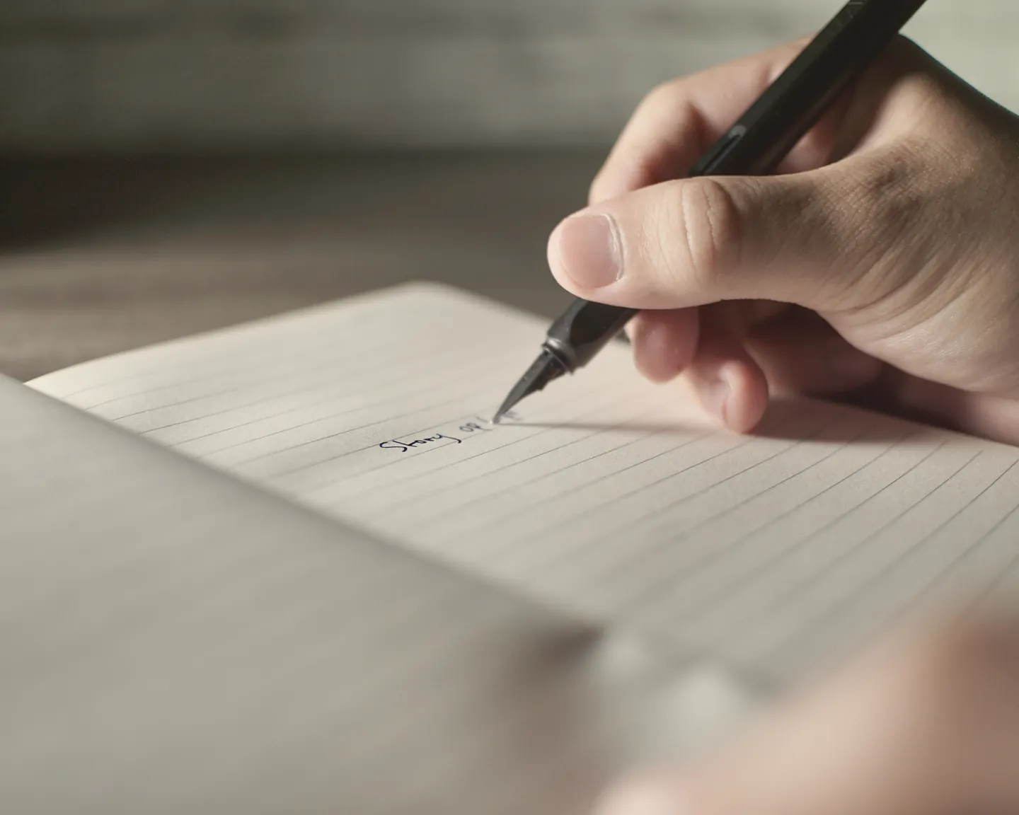 A hand writing in a lined notebook with a fountain pen